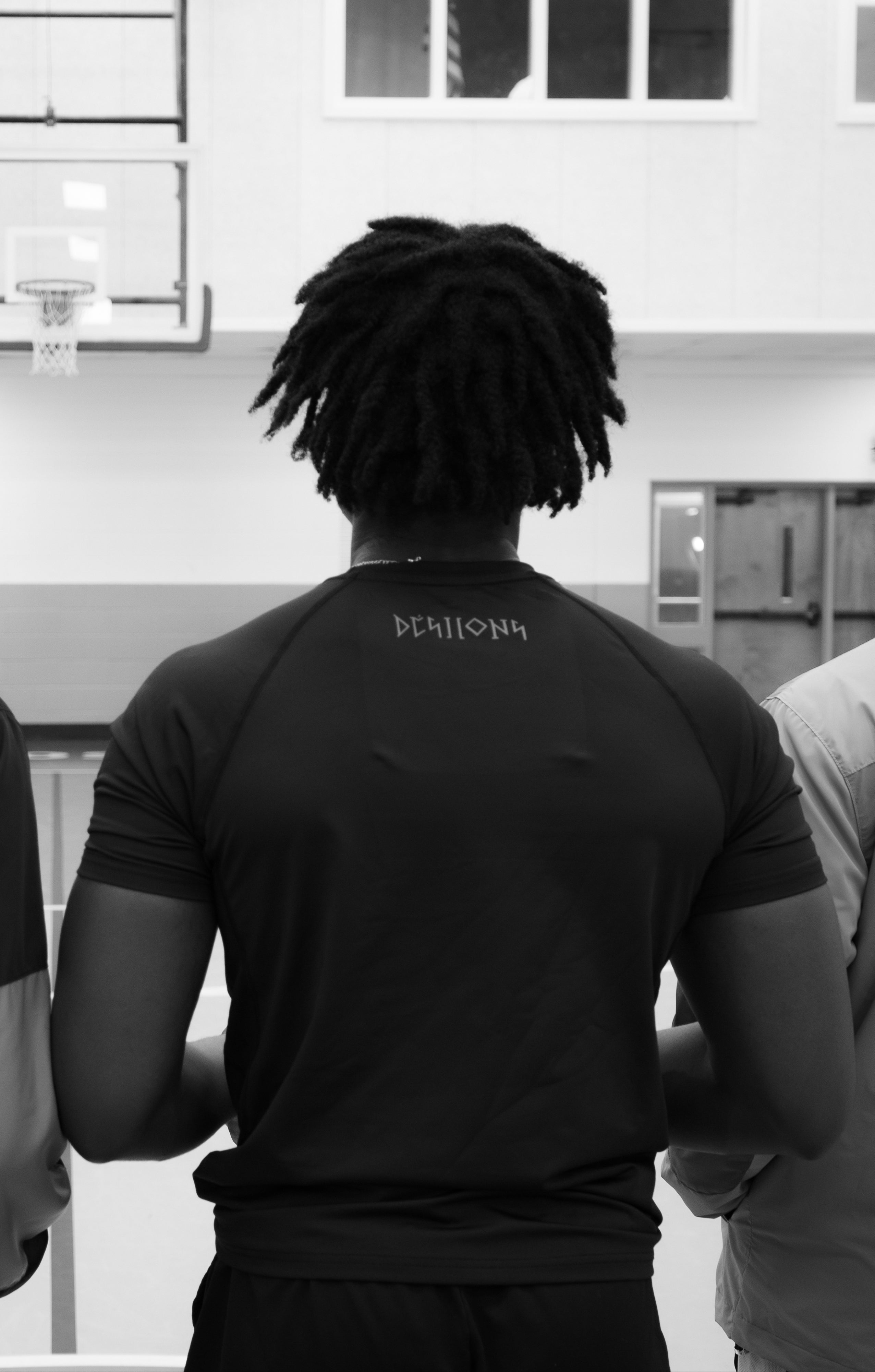 Four young men standing in a line, facing a basketball court with a cross on one of their shirts.